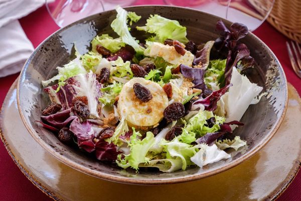 Mesclun-Salat aus grünen Blättern mit Ziegenkäse mit feinen Kräutern, Nüssen und Rosinen